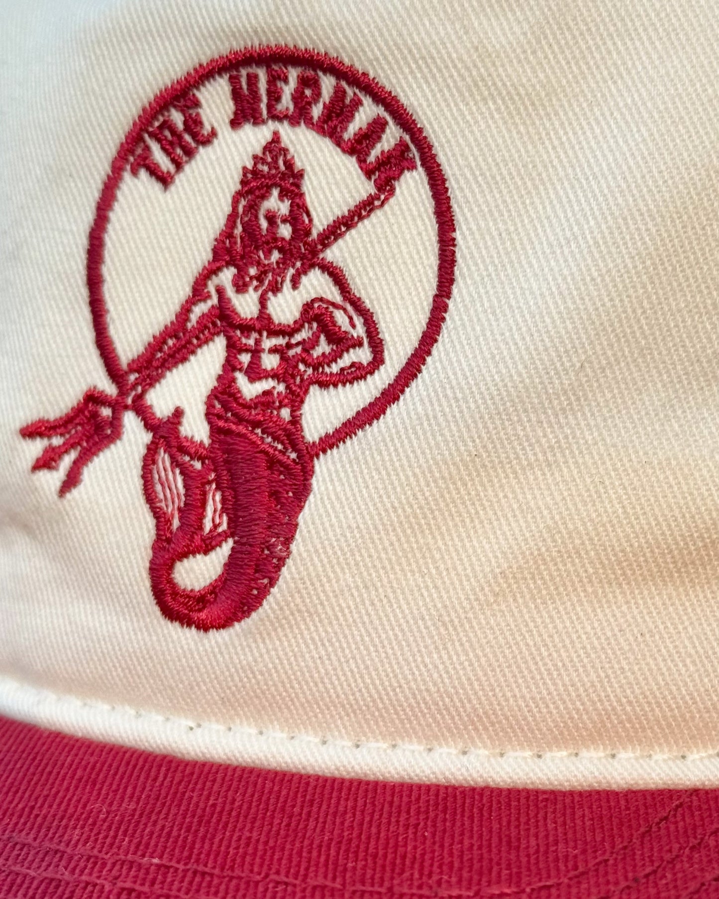 Baseball cap hat snap back with 'The Merman' logo embroidered in red on a cream off white canvas 