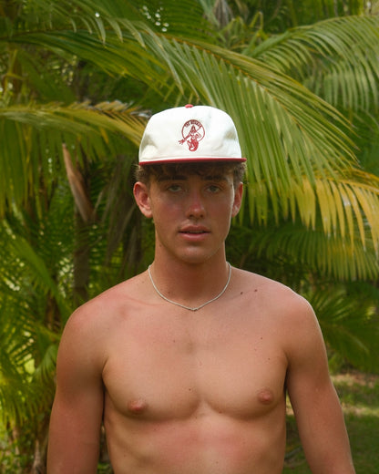 Man wearing a retro red and cream Merman baseball hat with embroidered Merman logo in front of palm trees